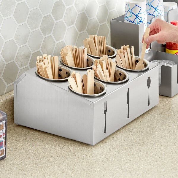 A hand holding a utensil from a stainless steel organizer with utensils.