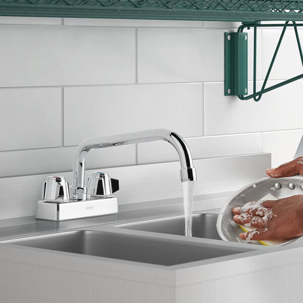 A person using a 1.8 GPM deck-mount faucet with 8" swing spout to wash dishes over a white sink.