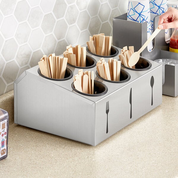 A silver container with black plastic cylinders holding wooden utensils.