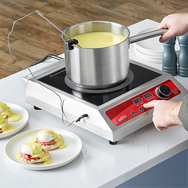 A person using a pot of liquid with a metal rod on an Avantco countertop induction range.