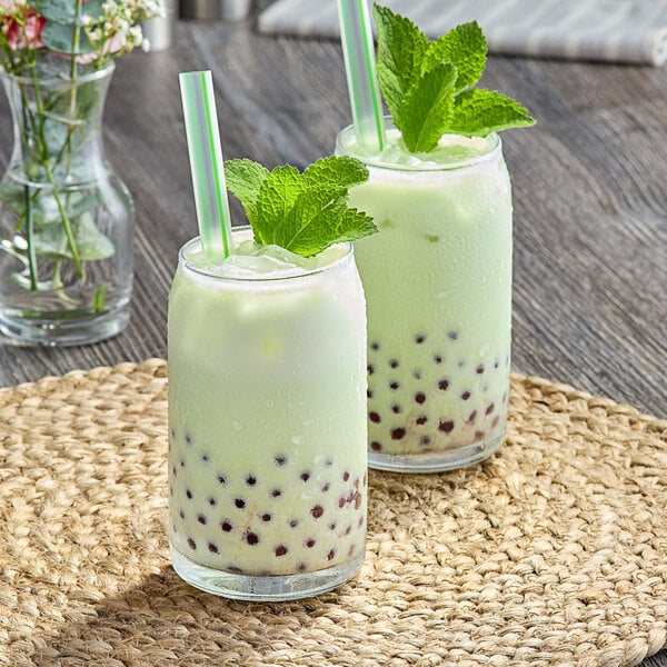 Two glasses of avocado bubble tea with straws and mint leaves.