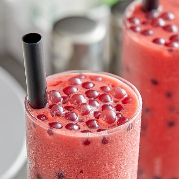 A glass of red liquid with Fanale Raspberry Popping Boba and a black straw on a white surface.