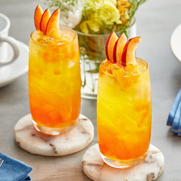 Two glasses of orange and yellow Fanale Mango smoothies with fruit slices on a table.