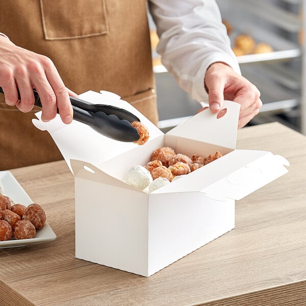 A hand holding a White Barn take out lunch box filled with doughnuts.