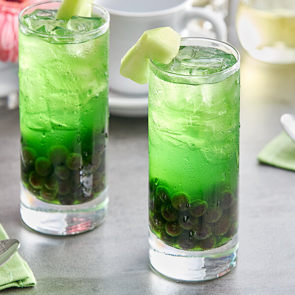 Two glasses of green Fanale Honeydew smoothie with fruit on a table.