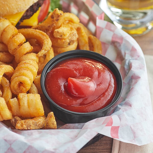 A cheeseburger and a basket of fries with a bowl of Red Gold tomato ketchup on a table.