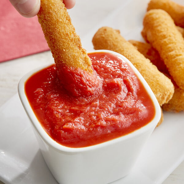 A person dipping a cheese stick into a bowl of Angela Mia pizza sauce.