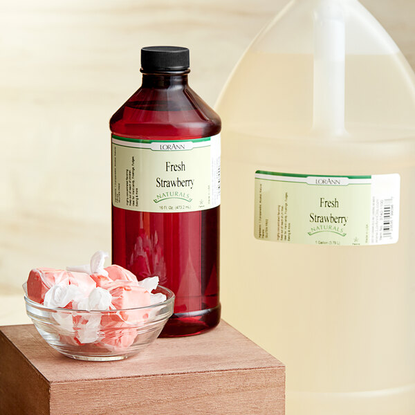 A jug of LorAnn Oils Fresh Strawberry natural flavor on a counter next to a bowl of candy.