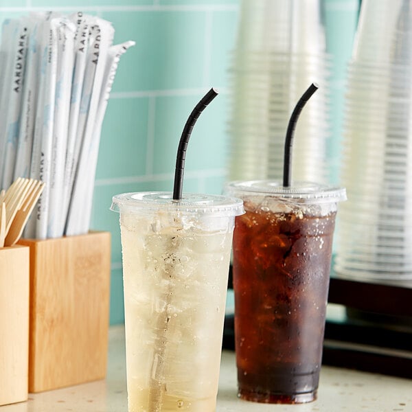 Two cups of brown liquid with Aardvark black paper straws on a table.