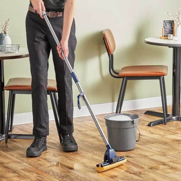 A person using a Lavex cellulose sponge mop to clean a wooden floor.