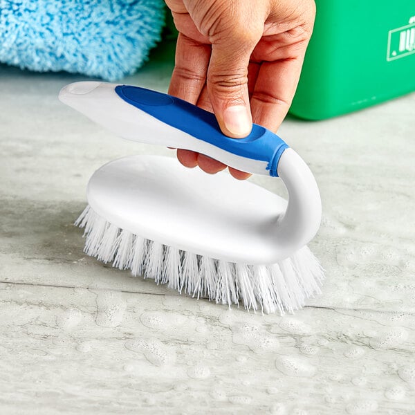 A person holding a Lavex iron scrub brush with polypropylene bristles.