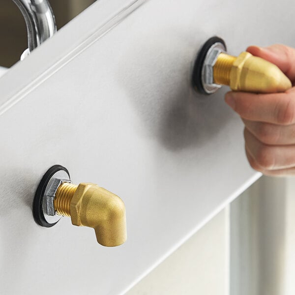 A person's hand using a Regency faucet installation kit to connect a gold pipe with a black ring to a sink.