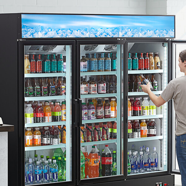 A man standing in front of a cooler with an Avantco Blue Graphic Sign Panel for GDC-69-HC on it.