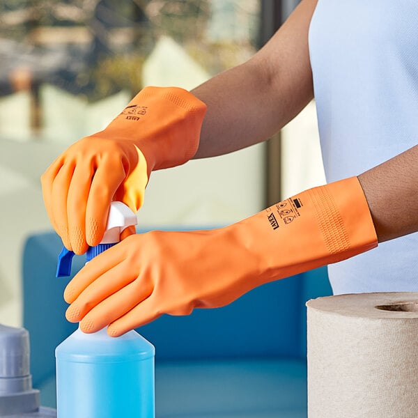 A person wearing orange Lavex gloves using a spray bottle.