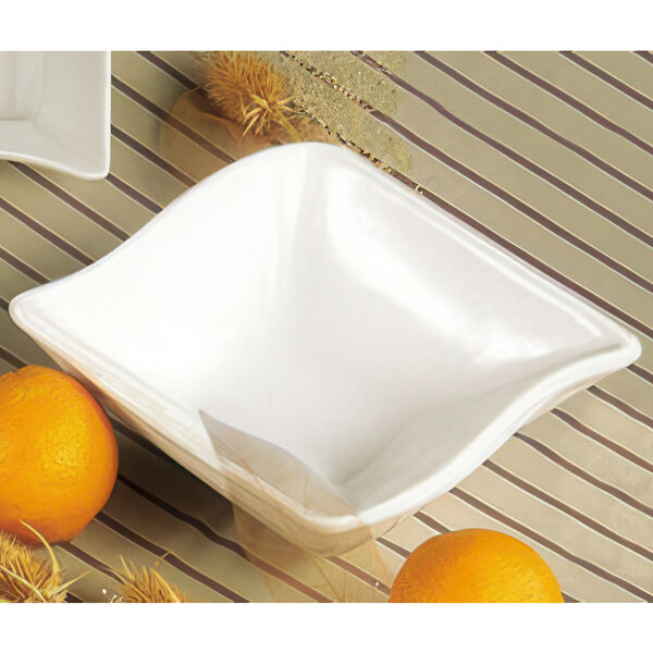 A white square CAC Soho stoneware bowl with oranges on a striped table.