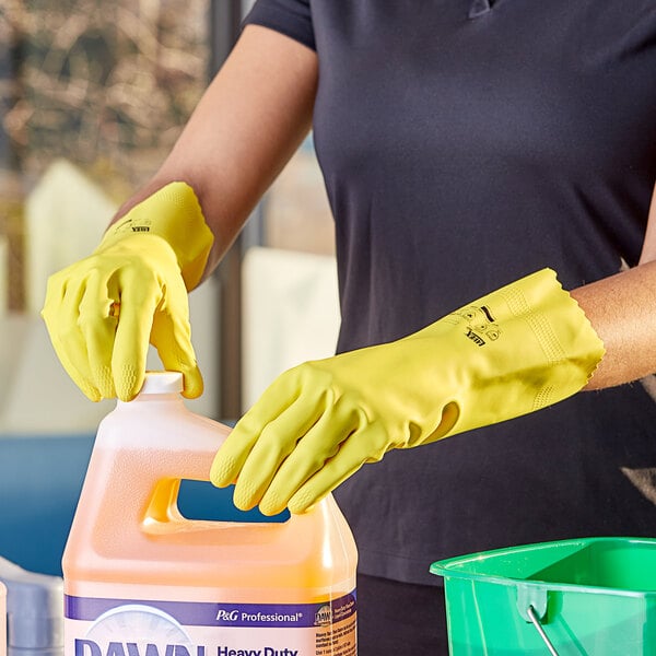 A person wearing Lavex yellow rubber gloves holds a jug of cleaning liquid.