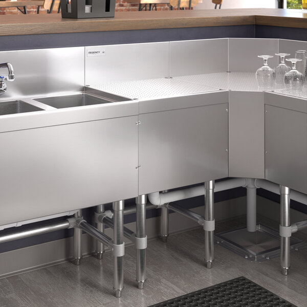 A Regency stainless steel underbar drainboard on a stainless steel counter above a stainless steel sink.