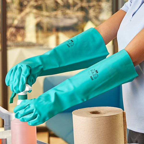 A woman wearing Lavex green unlined nitrile gloves cleaning a roll of toilet paper.