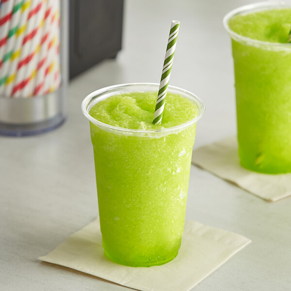 A plastic cup of green Original Slushie Company Sour Apple slushy with a straw.