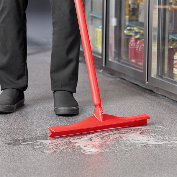 A person using a Vikan red single blade rubber floor squeegee to clean the floor.