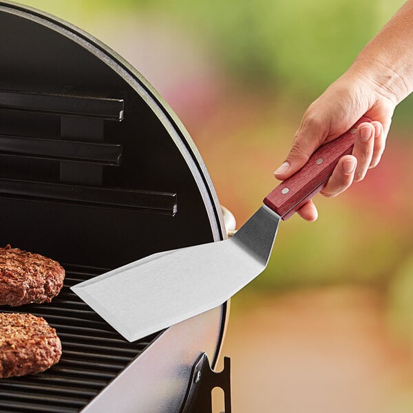 A person using an American Metalcraft solid turner to flip a burger on a grill.