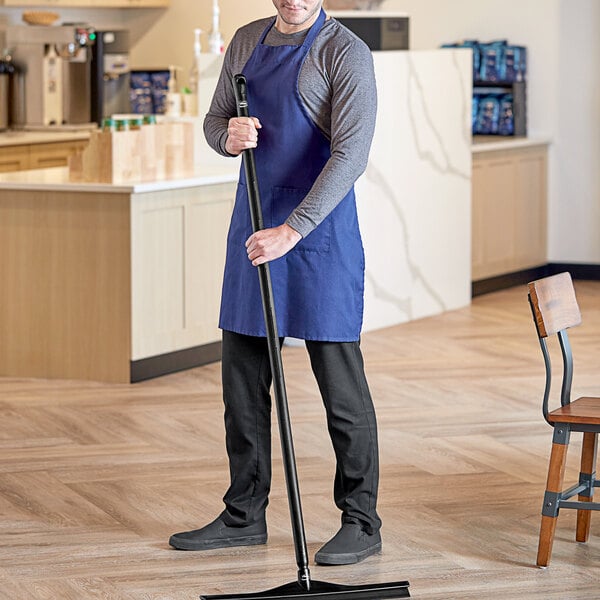 A man in a blue apron holding a black pole with a Vikan Ultra-Hygienic Handle.