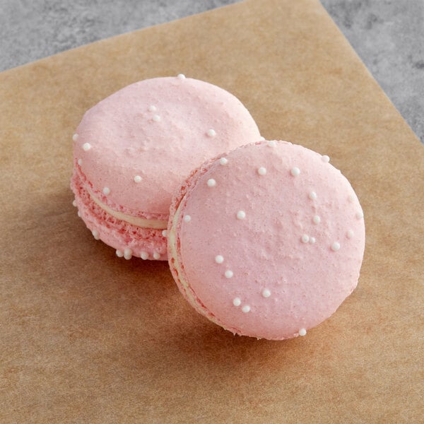 Two pink Macaron Centrale peppermint raspberry macarons on a brown surface.