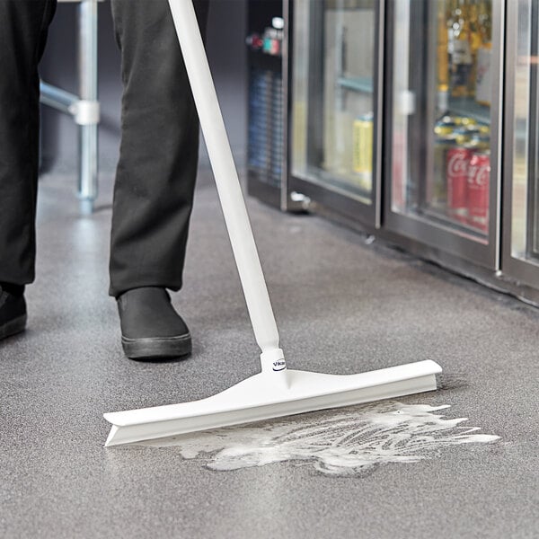 A person using a white Vikan Ultra-Hygienic single blade rubber floor squeegee to clean a floor.