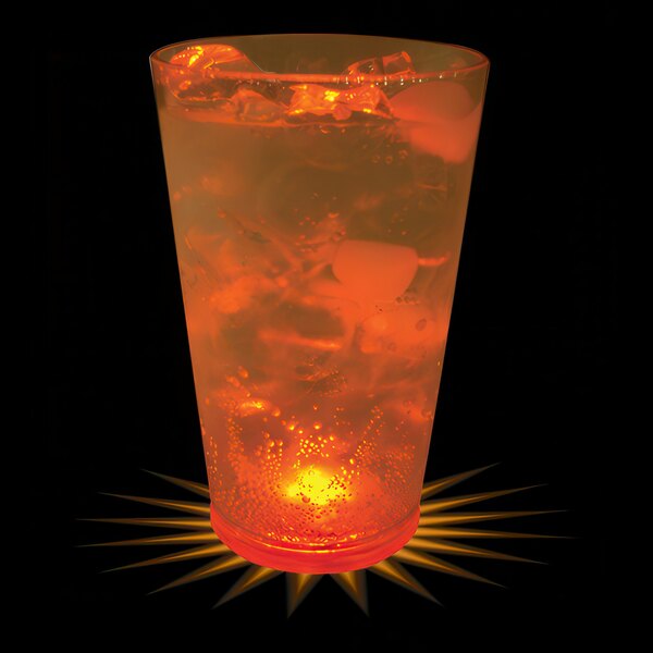 A customizable plastic pint cup with an orange LED light in a glass of orange liquid with ice.