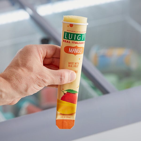 A hand holding a yellow Luigi's Mango Italian Ice tube.