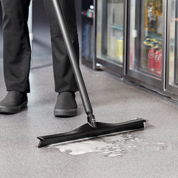 A person cleaning a floor with a Vikan black single blade rubber floor squeegee.