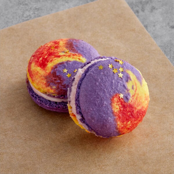 Two raspberry pineapple macarons with colorful designs on them.