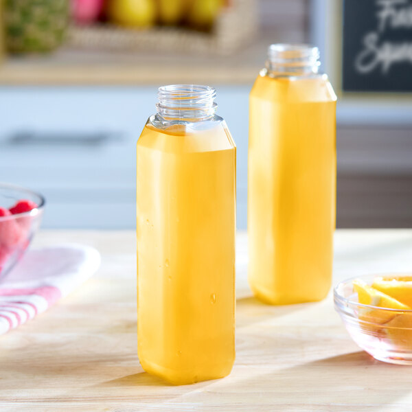 A pair of clear, tall square plastic juice bottles filled with a yellow liquid, placed on a kitchen counter.