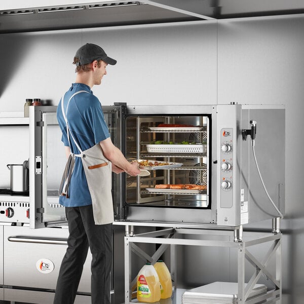A person wearing an apron putting food into a Cooking Performance Group electric combi oven.