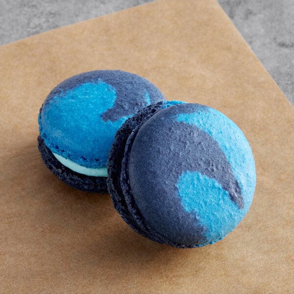 Two blue and black Macaron Centrale Blue Curacao macarons on a brown surface.