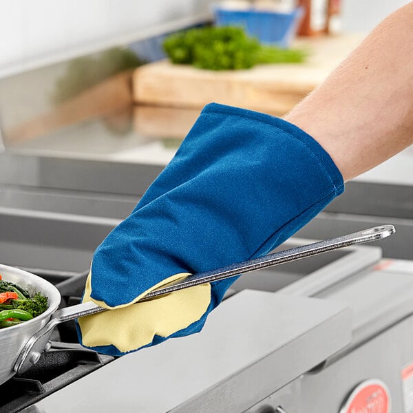 A person using a Tucker Safety oven mitt to hold a pan over a stove.