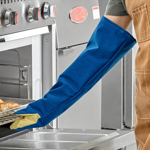 A person wearing a Tucker Safety blue and yellow oven mitt holding a tray of food.