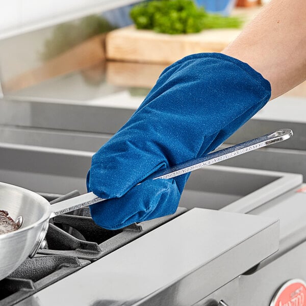 A person wearing a Tucker Safety blue Nomex oven mitt holding a pan over a stove.