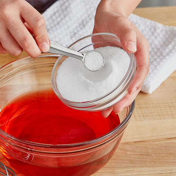 A spoon with a white powder (Regal Synthetic Tartaric Acid) over a bowl.