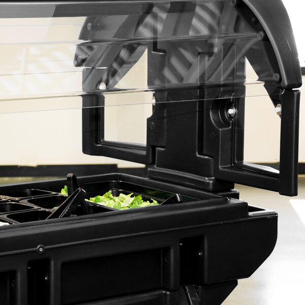 A black Cambro food and salad bar container with a clear plastic lid filled with lettuce.