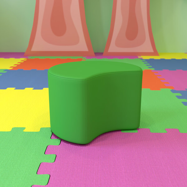 A green flexible soft seating moon ottoman on a colorful surface.