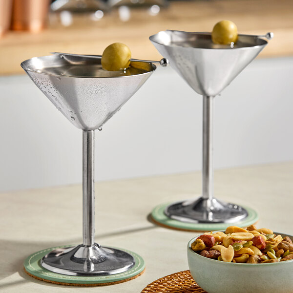 Two Franmara stainless steel martini glasses filled with olives on a counter in a cocktail bar.