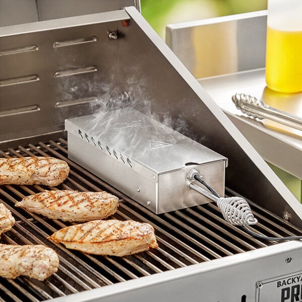 A Cooking Performance Group smoker box on a grill with grilled chicken and meat.