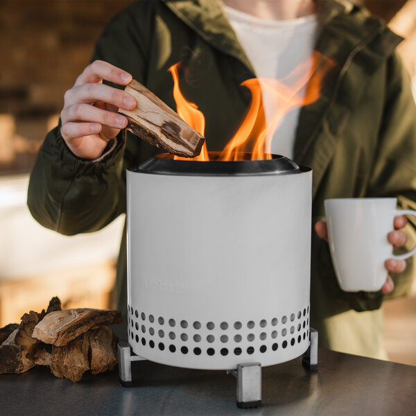 A woman putting wood into the fire in a white Solo Stove Mesa XL.