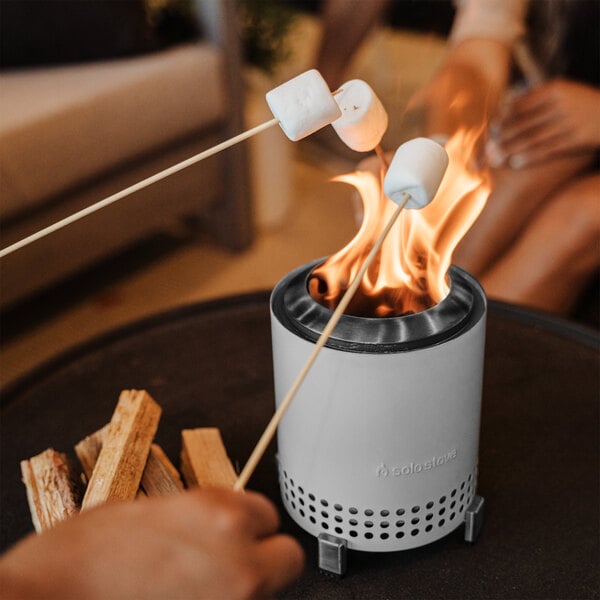 A person roasting marshmallows on sticks over a Solo Stove Mesa fire pit.
