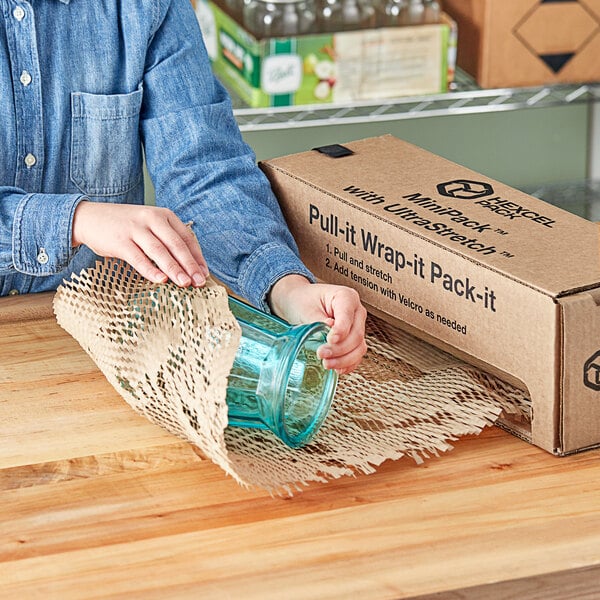 A woman using HexcelWrap MiniPack to put a glass jar in a box.