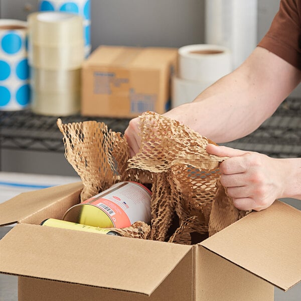 A person opening a cardboard box with a HexaFil Expanding Void Fill Paper Dispenser inside.
