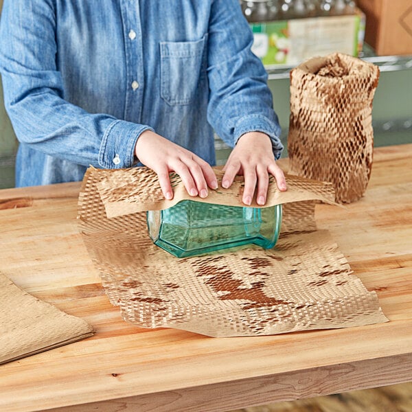 A person wrapping a glass jar with HexcelWrap paper on a table.