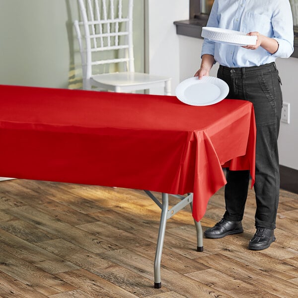 A woman standing at a table with a red plastic tablecloth on it.