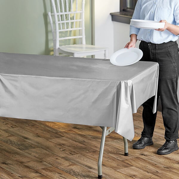 A woman holding a white paper plate over a metallic silver plastic table cover on a table.